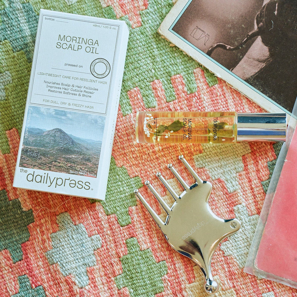 Moringa scalp oil bottle with packaging and a comb on a textured surface