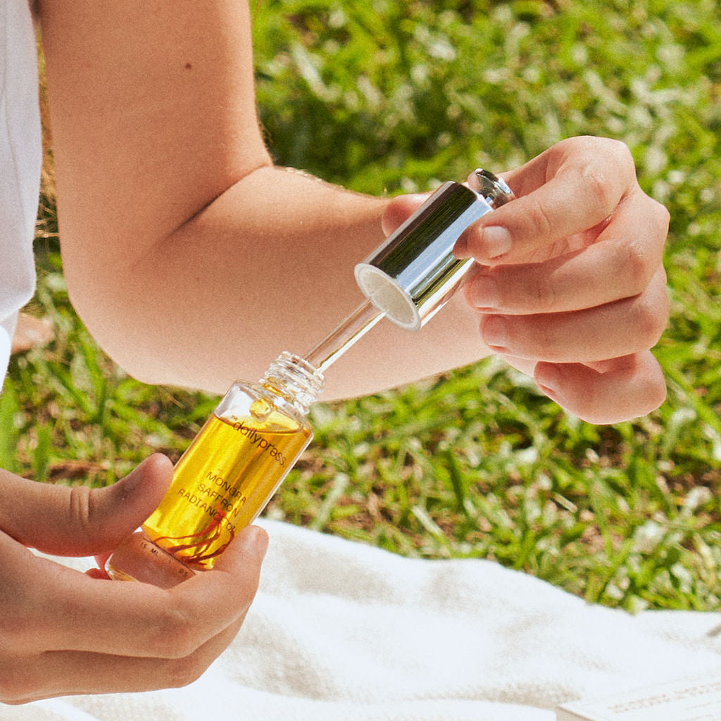 Person holding a dropper bottle outdoors on a grassy background