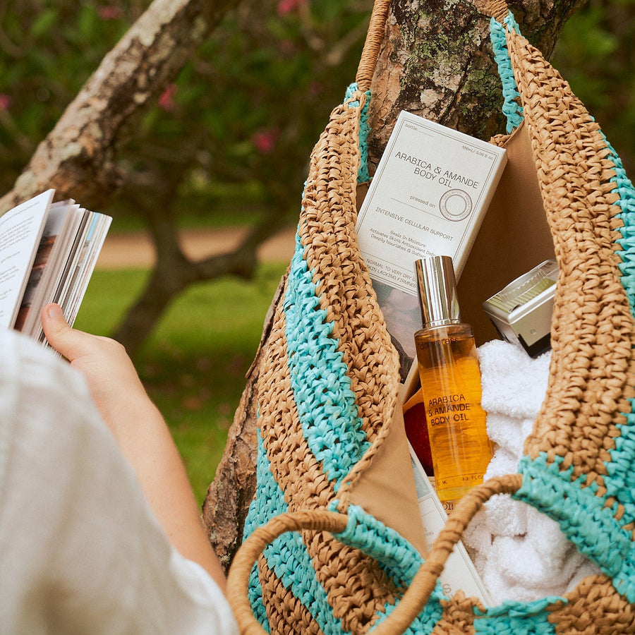 Person reading a book with a crocheted bag hanging on a tree branch outdoors