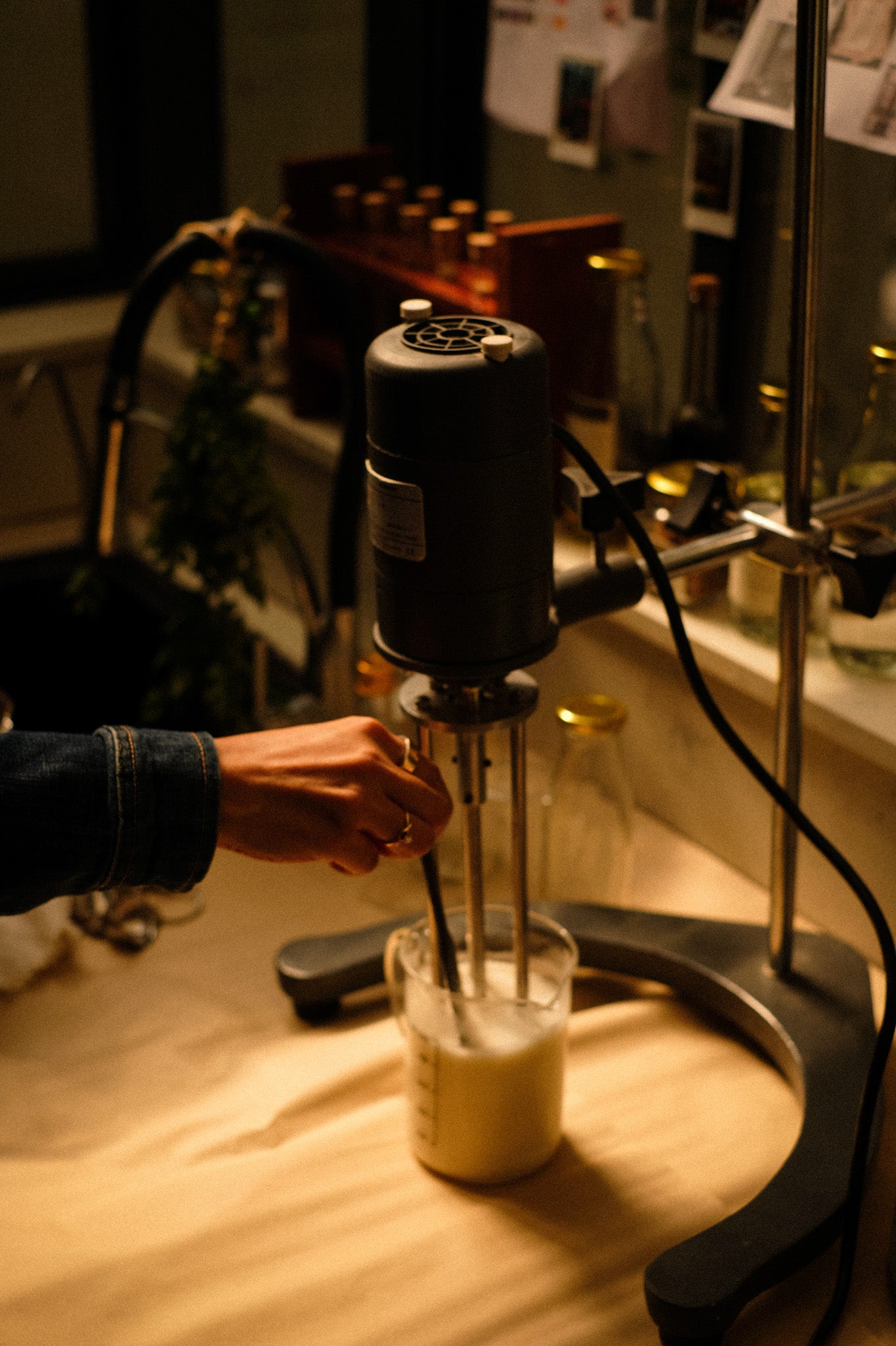 Person using a homogeniser in a lab setting with various items in the background.